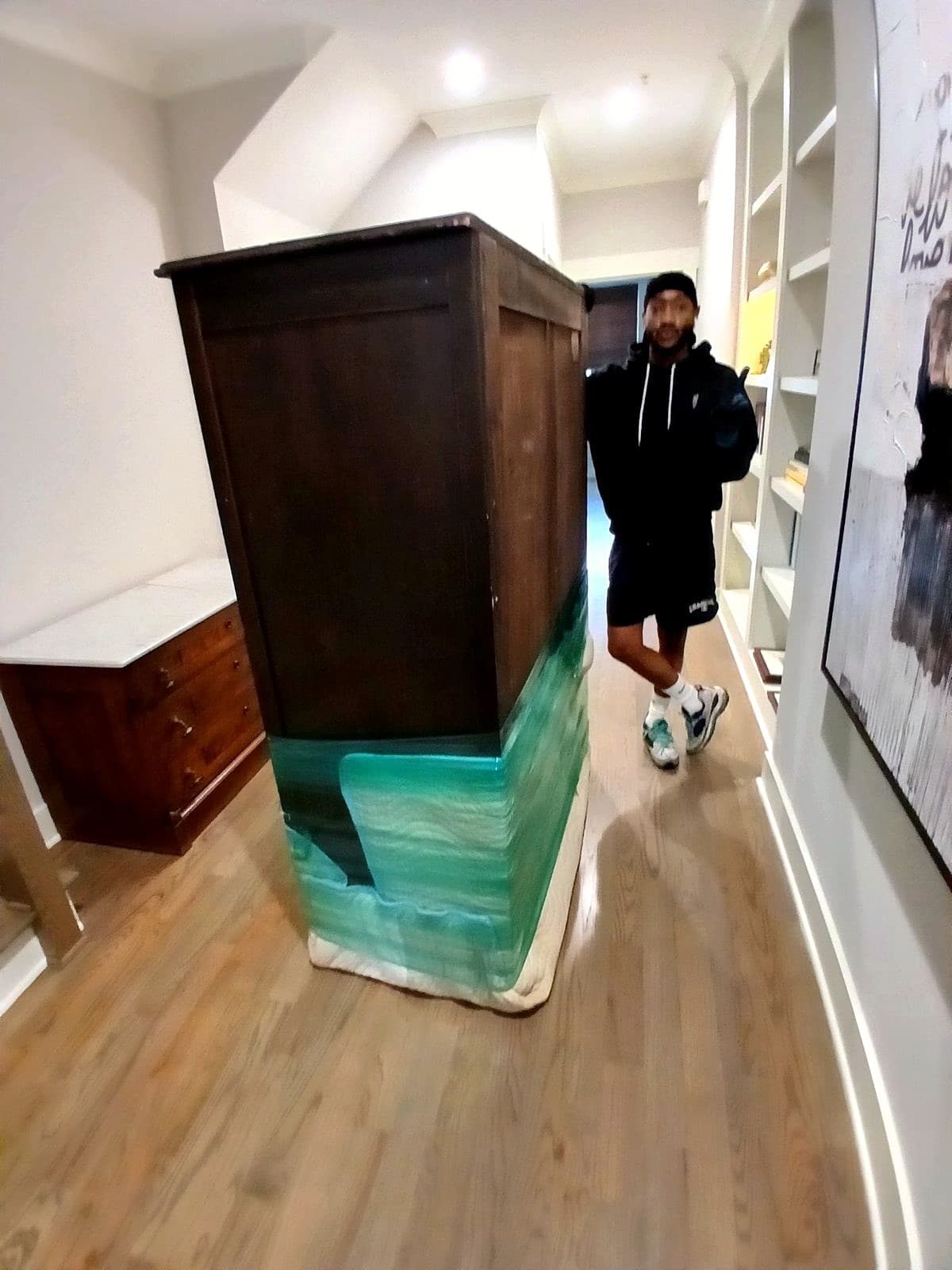 Quez carrying a tall dark wood armoire through a home.