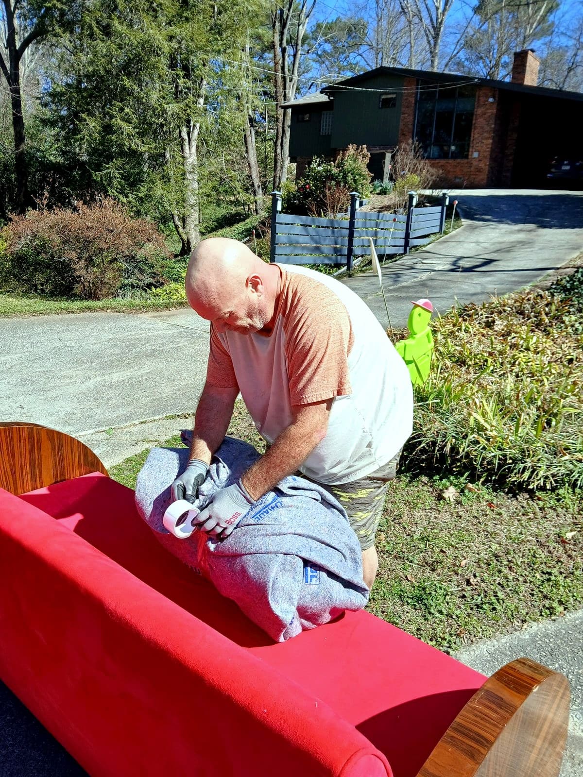 Gary wrapping a red sofa in moving blankets outside a home.